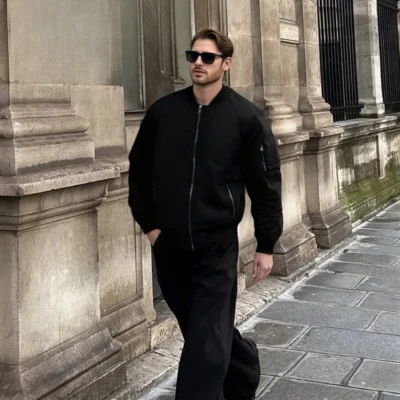 Model in black waterproof bomber jacket walking outdoors, designed for travel, urban commuting, and light outdoor use.