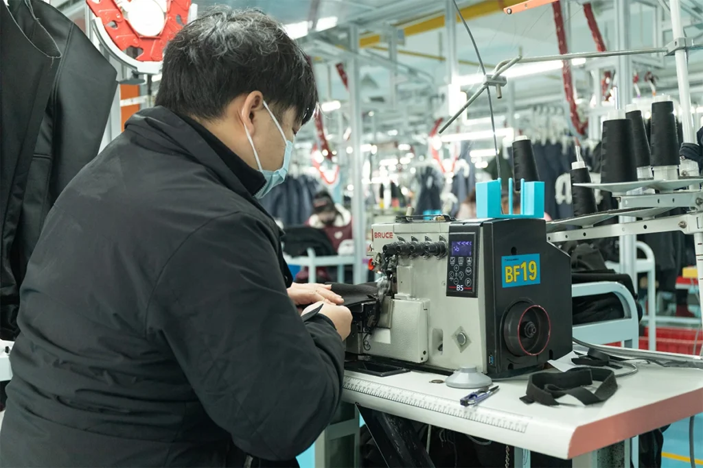 Technician sewing outdoor winter jackets on automated production line inside OEM factory – Fronter Group
